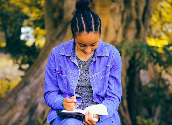 Young woman sitting outside and taking notes in her agenda