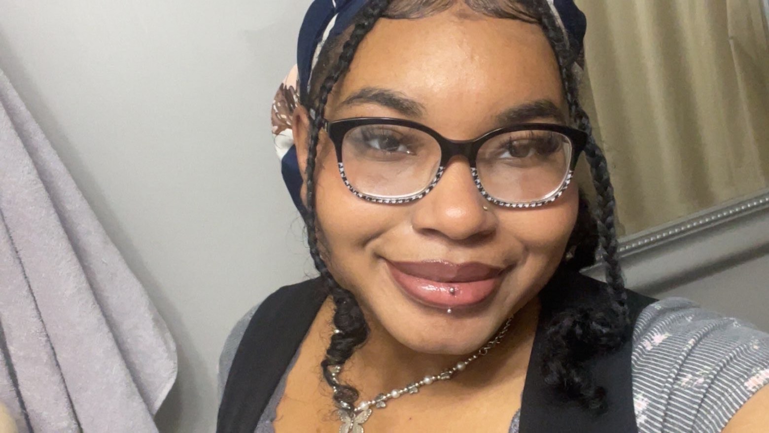 Toni in an up-close selfie smiling. Toni wears black glasses and has a lip piercing.