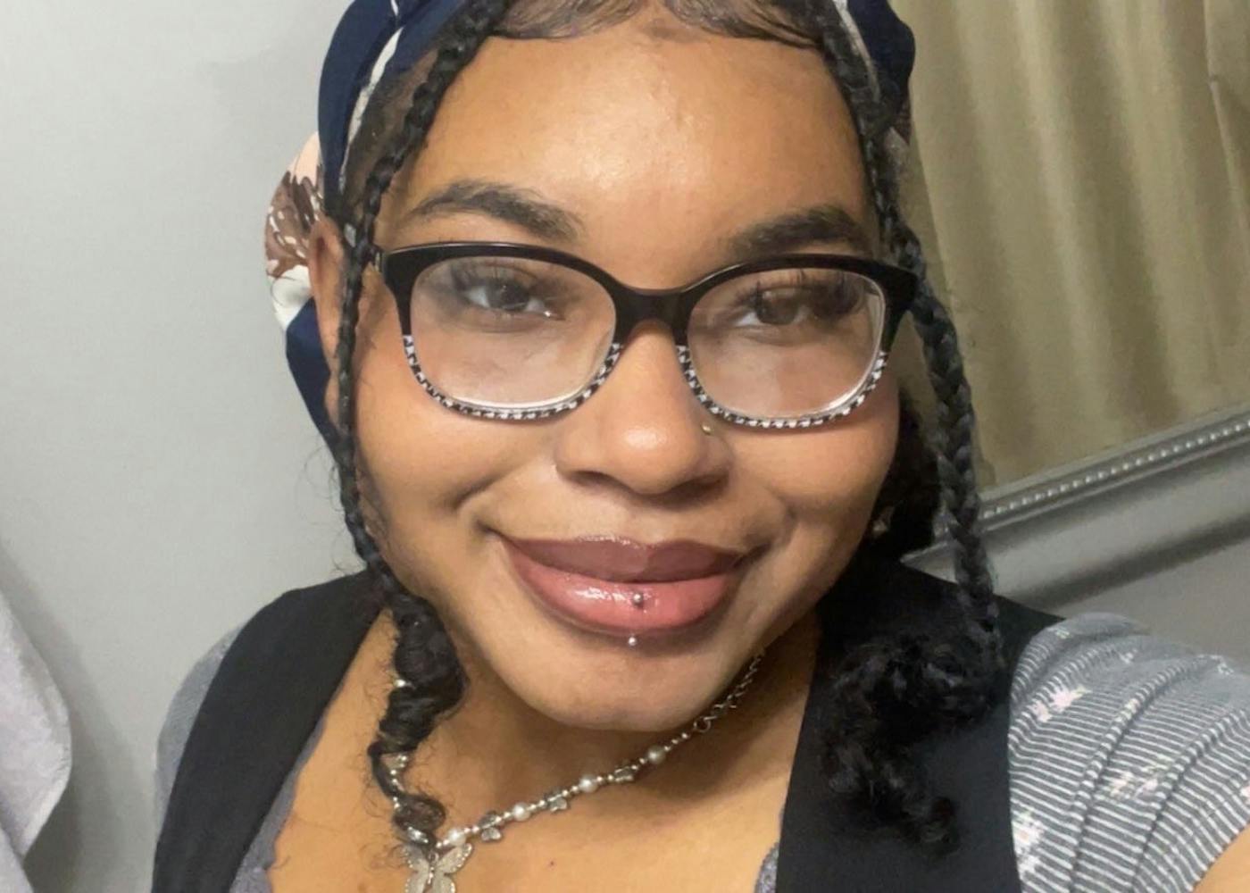 Toni in an up-close selfie smiling. Toni wears black glasses and has a lip piercing.