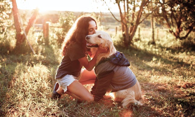 Young teen girl kissing her Golden Retriever dog in a garden.