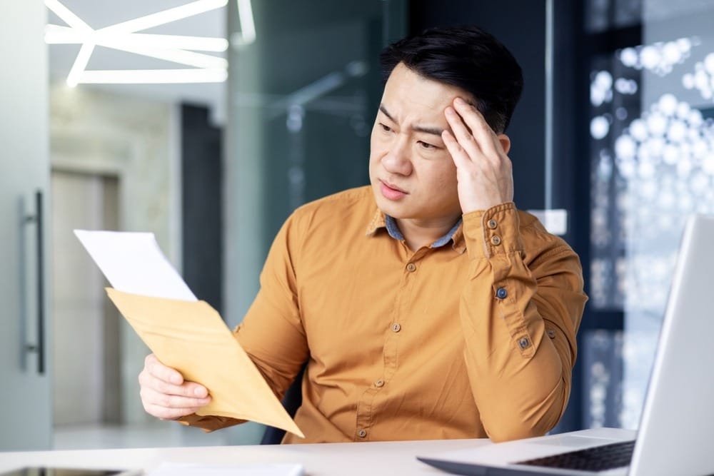 Man looking worried while viewing his computer and a bill.