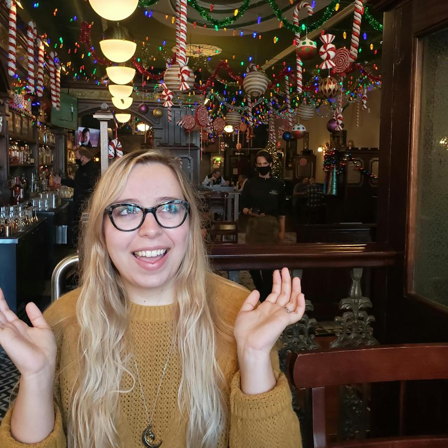 Addie gestures with her hands up at a bar decorated for Christmas.