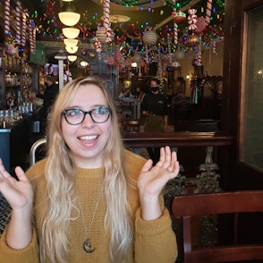 Addie gestures with her hands up at a bar decorated for Christmas.
