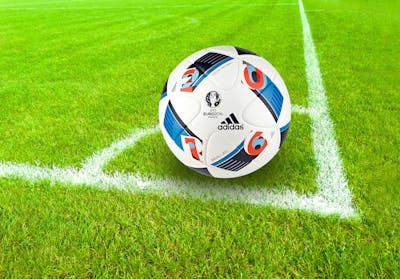 Official Euro 2016 soccer ball on green field with white boundary lines. Adidas ball features blue and red design elements on white background.