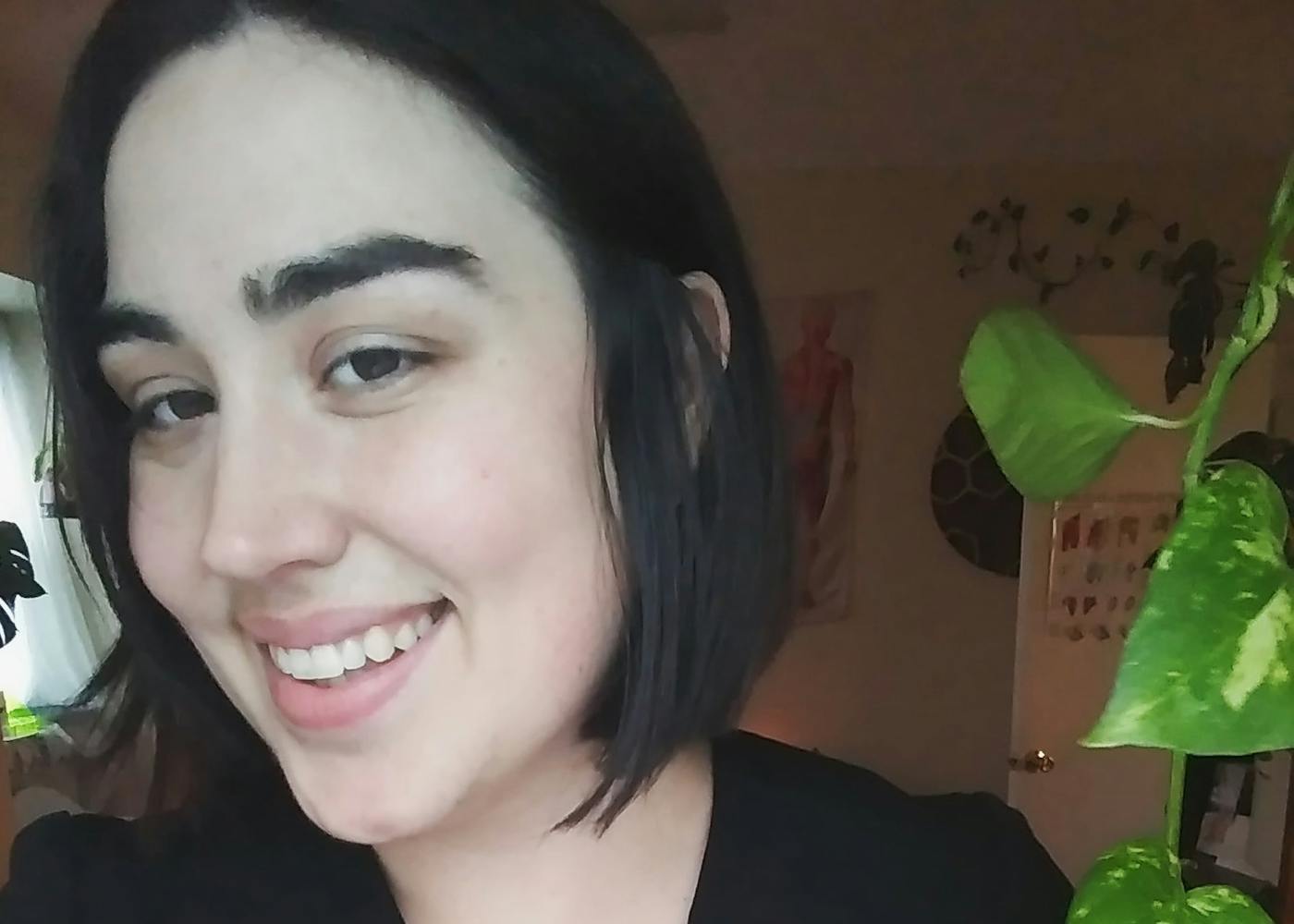 Courtney, a white woman dressed in black massage therapist scrubs, smiles.