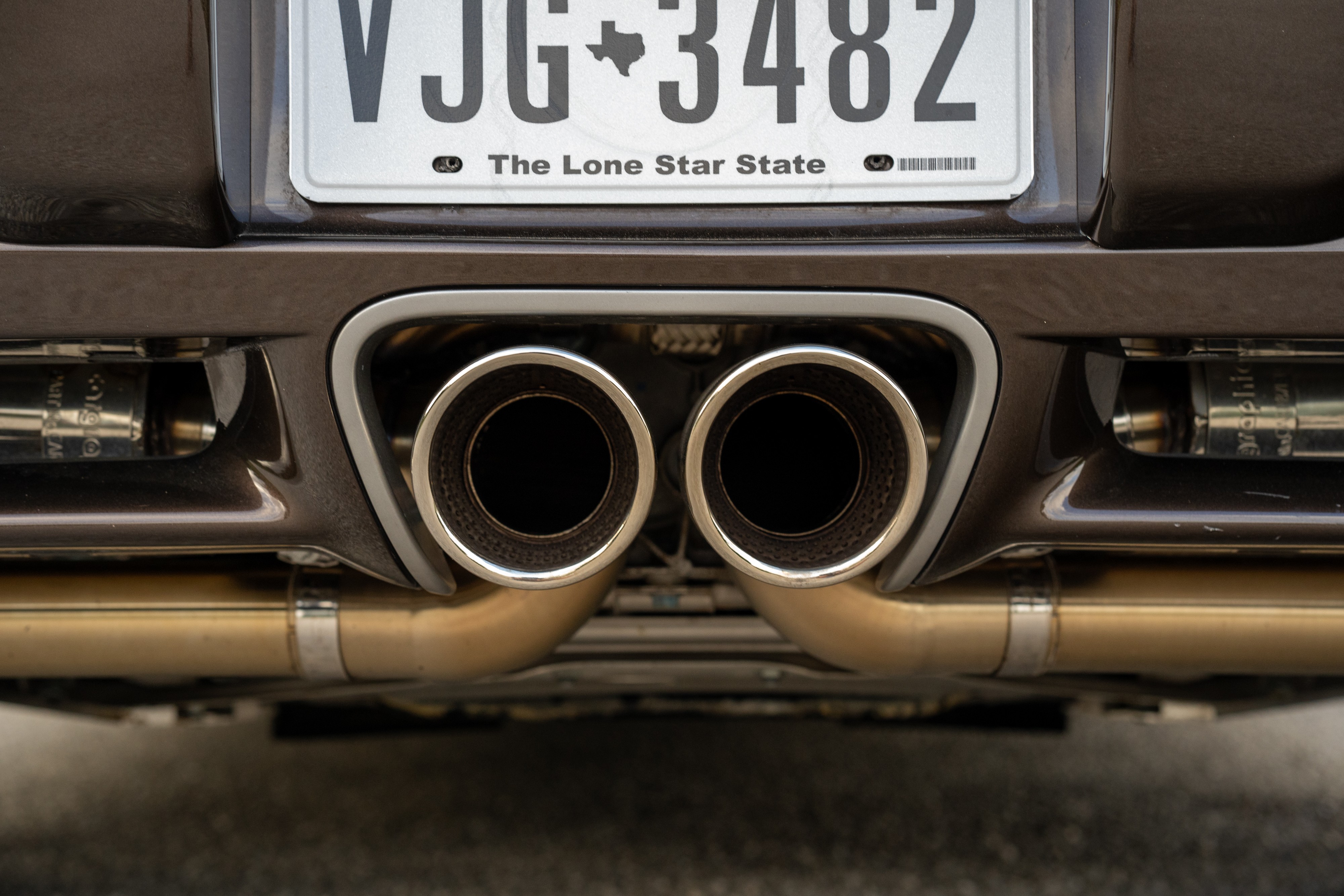 Modified exhaust on a 2008 Porsche Cayman S in Macadamia Metallic on Brown.