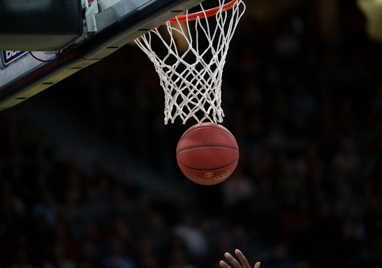 Basketball dropping cleanly through the hoop during a live game, with the net stretched and crowd blurred in the background.