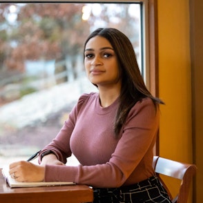 Leticia sits at a table with a pen and notebook in hand as she prepares to copyedit.