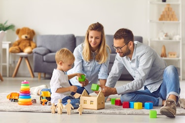Happy mom, dad, and toddler playing at home with blocks and a toy house.