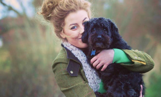 Blond woman holding a cute black doodle puppy