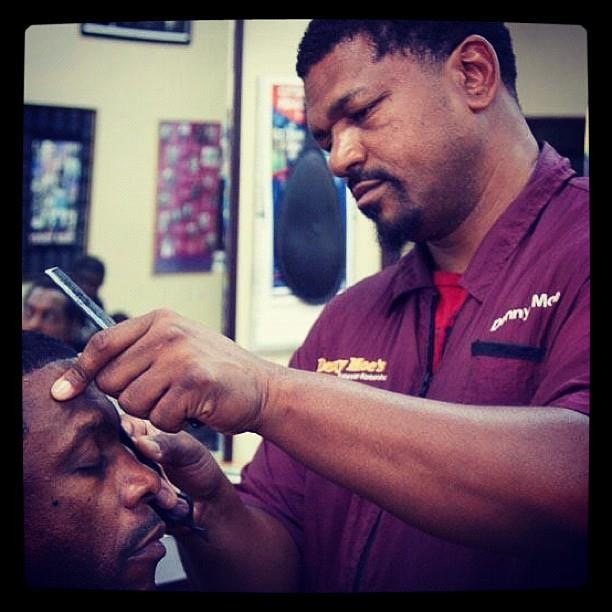 Denny, dressed in a red shirt, concentrates on styling a client's hair.