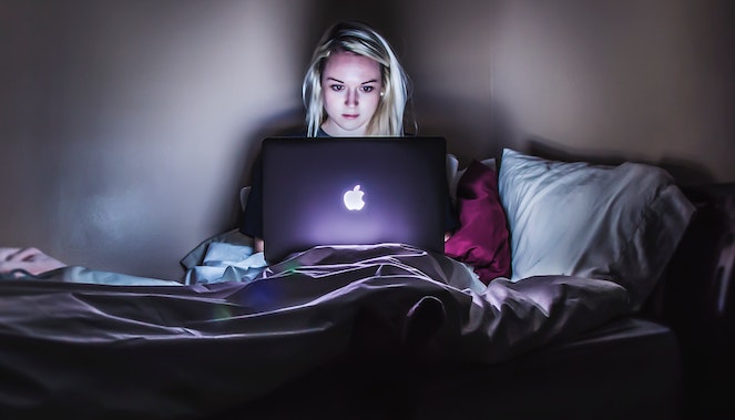 Young woman sitting up in bed on her laptop at night