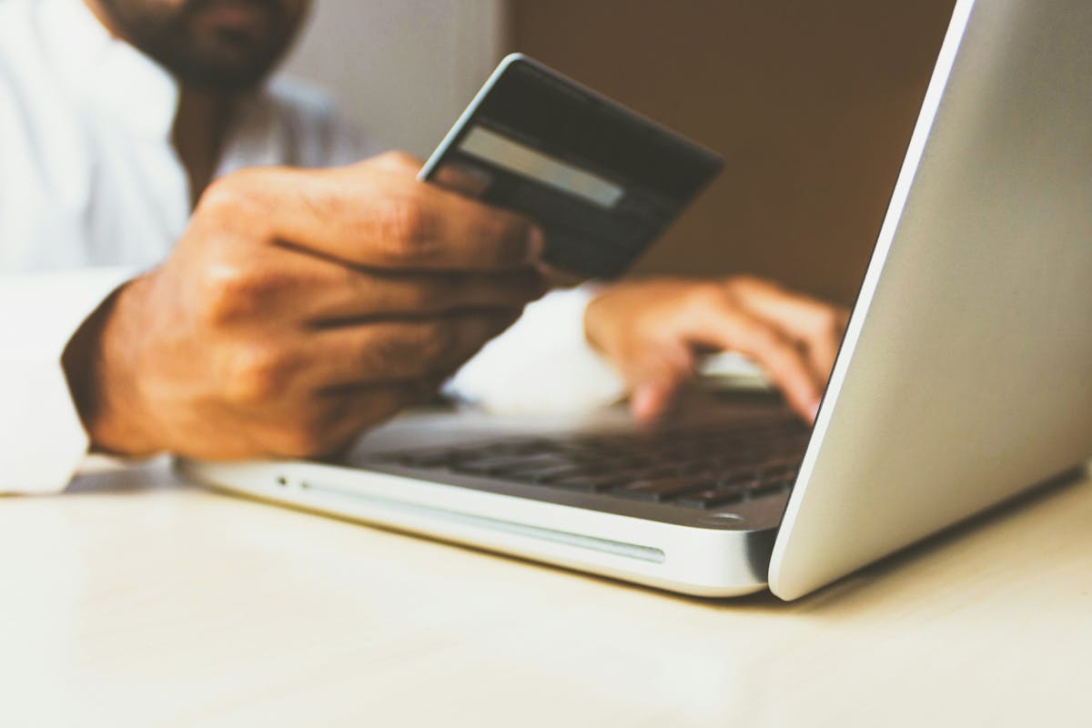 A person holding a dark credit card while typing on a laptop, suggesting online shopping or a digital financial transaction.