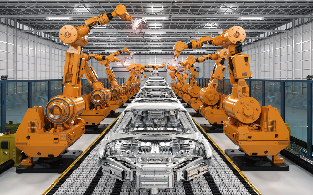 Large orange robotic arms work on a manufacturing conveyor belt to build parts.
