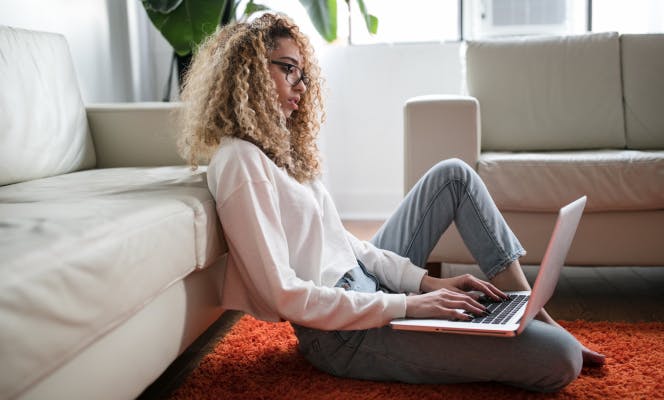 Young woman with curly blond hair laying on the couch and browsing her laptop