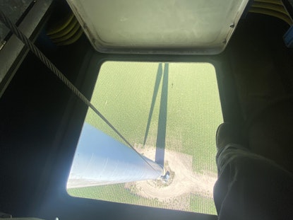 A small window within a wind turbine that looks down all the way to the grass below.