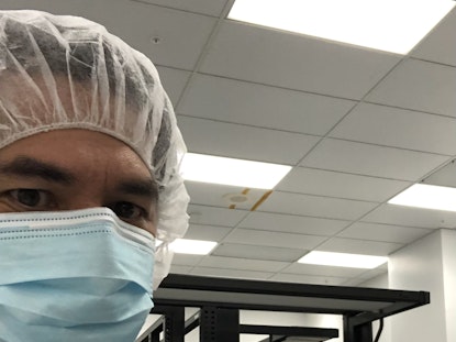 David, dressed in a white lab coat, carefully inspects a Mars rover airbag retraction system. The airbag helps the rover land safely.