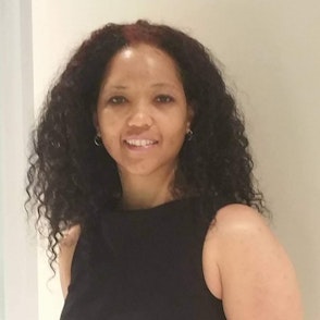 Desiré, a black woman in her 50s wearing a black blouse, smiles in her office.