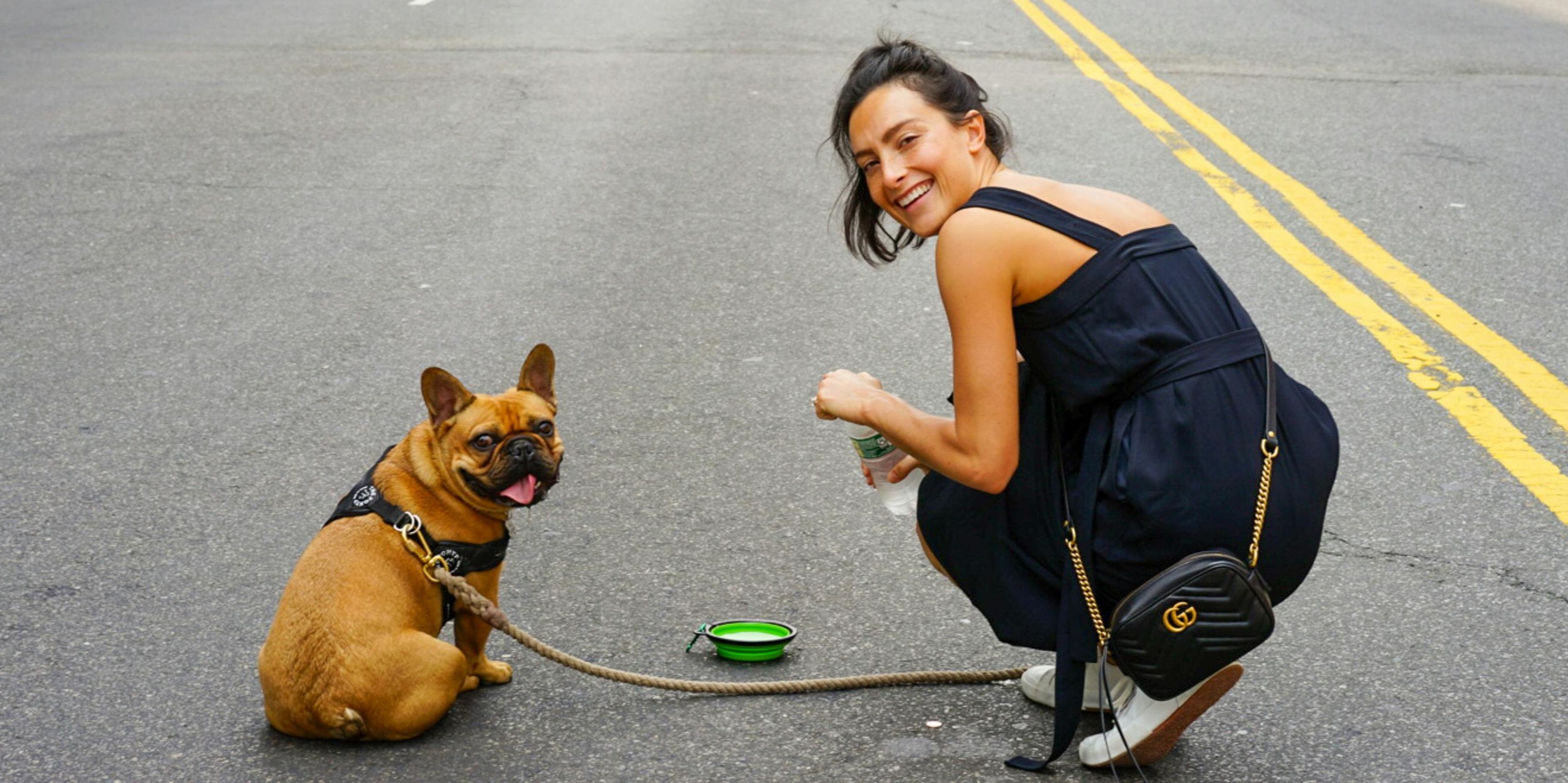 brown french bulldog sitting on street with young female owner