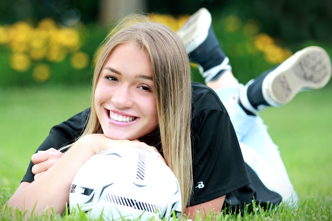 Young woman smiling, lying in the grass and resting her chin on a soccer ball