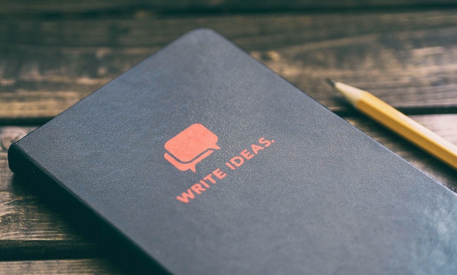 Leather idea book sitting on wooden table next to a pencil