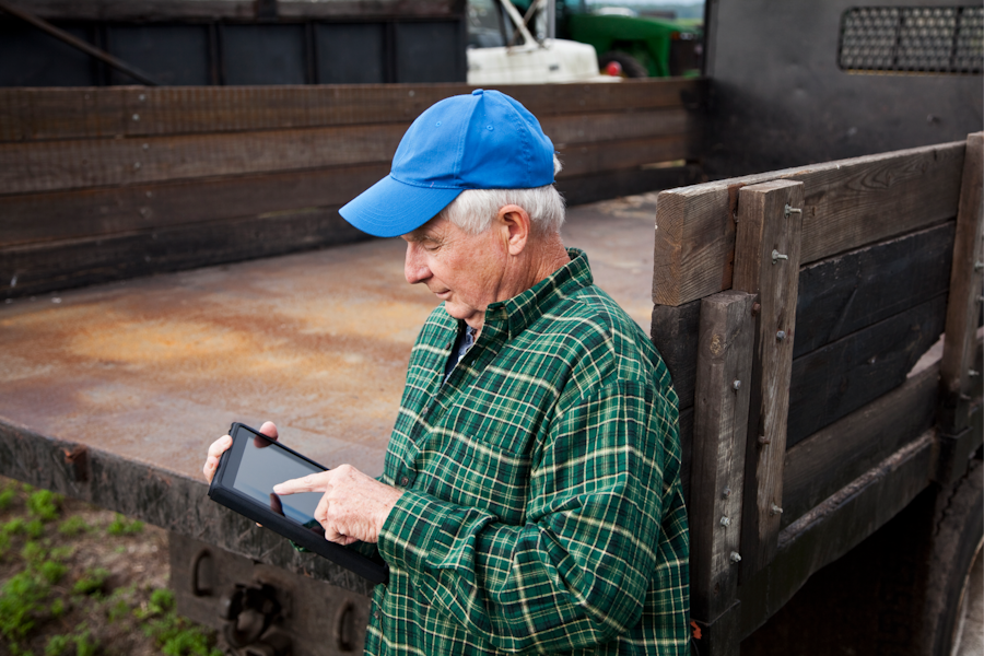 Old man using a tablet leaning against a work truck