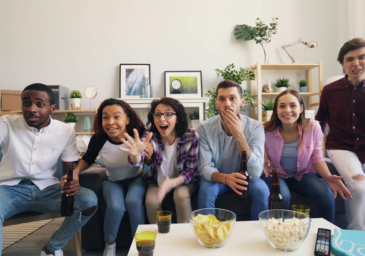 Group of friends watching a sports game on TV, reacting with excitement and surprise.