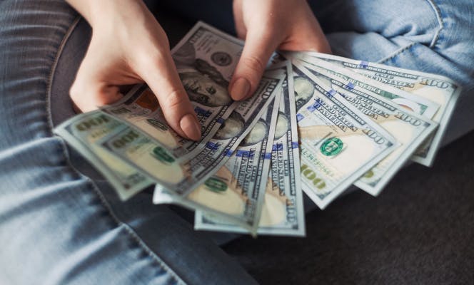 Woman holding 100 dollar bills fanned out in her hands. 