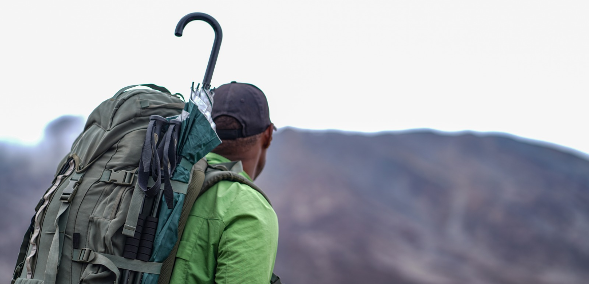 Trekker-with-backpack-and-umbrella-on-Kilimanjaro-climb---The-Adventure-People.png