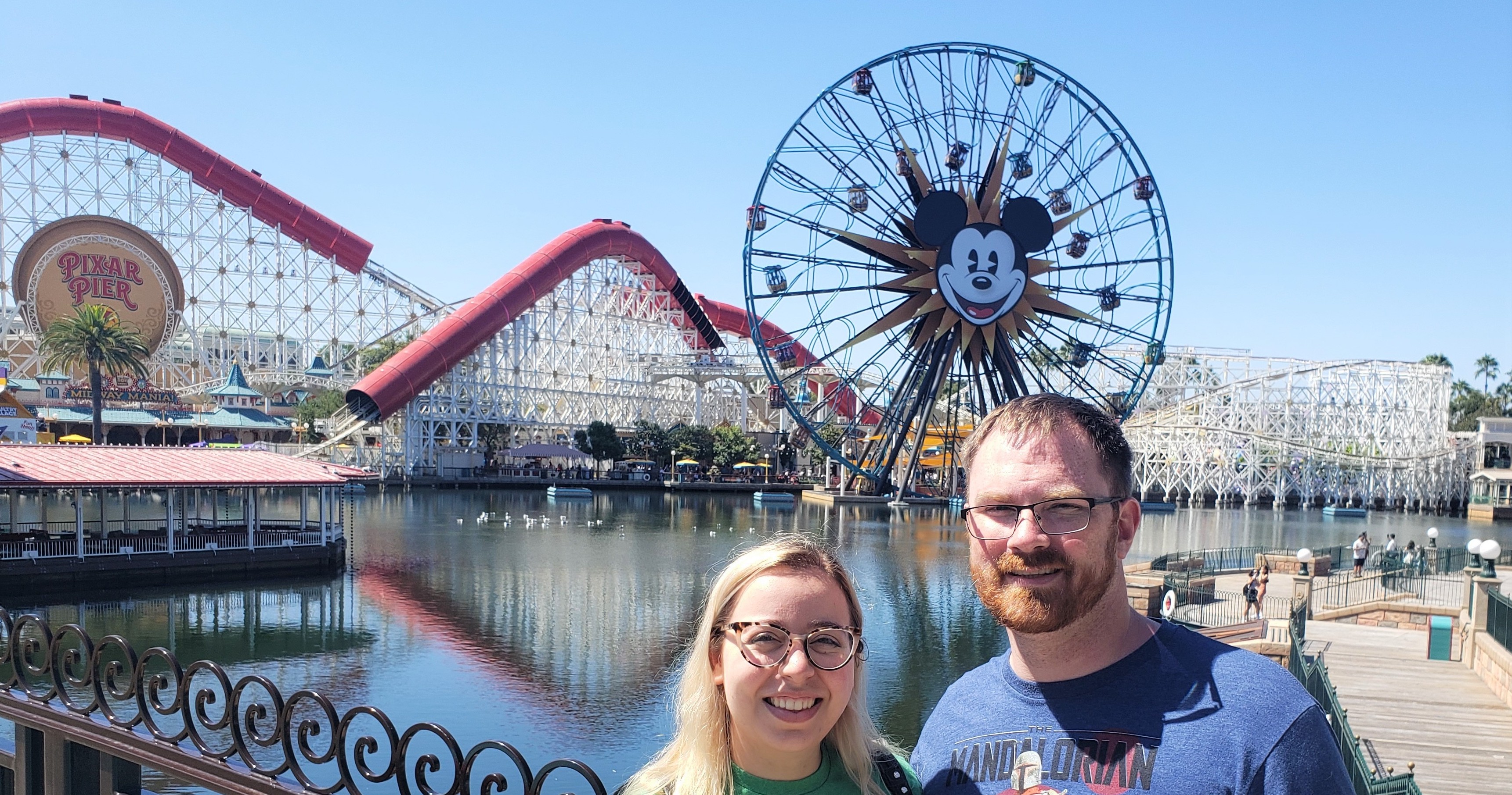 Addie and another man pose in front of a roller coaster and Ferris wheel at Disney California Adventure Park.