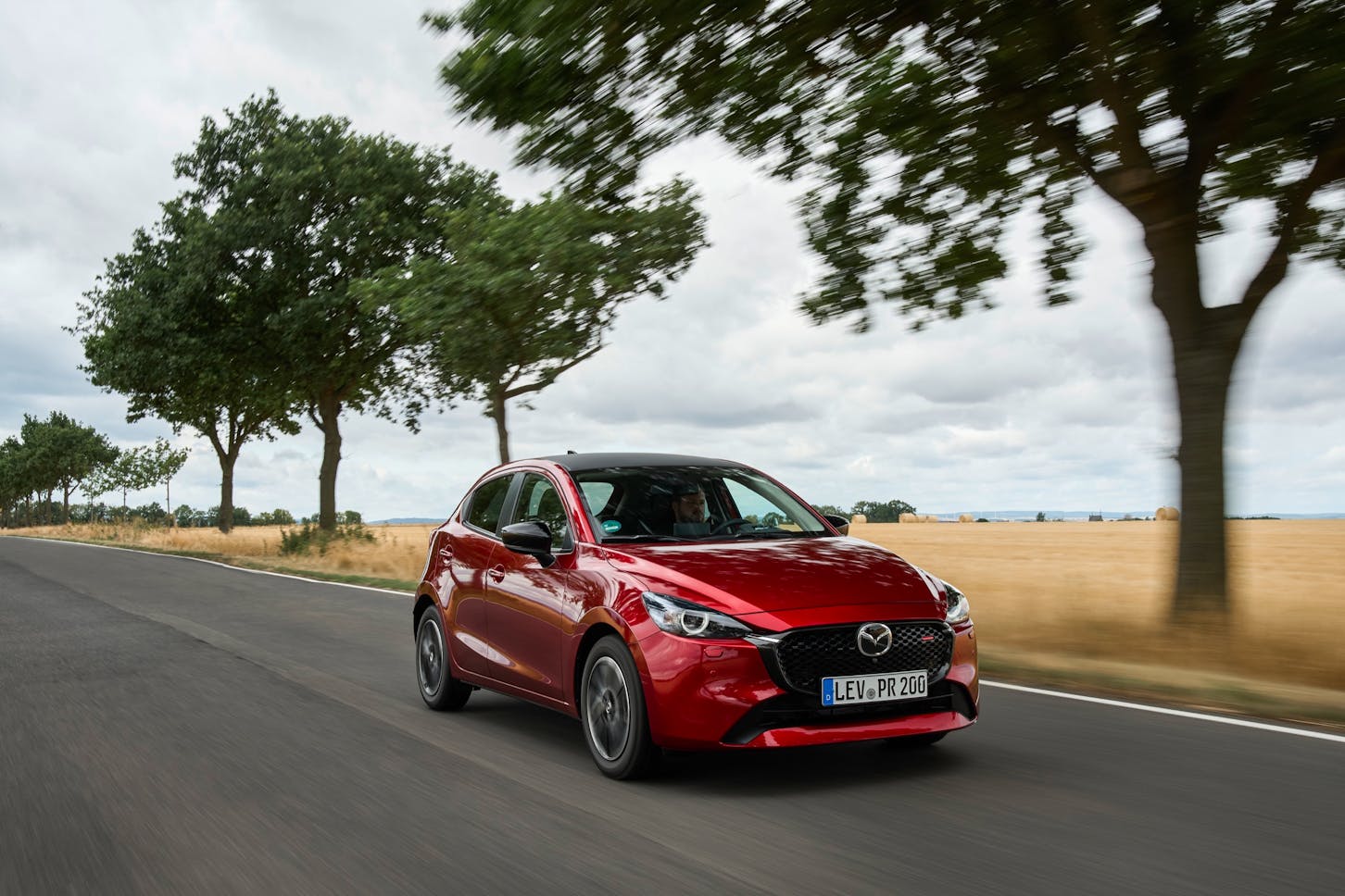 Ein roter Mazda2 Hybrid fährt auf einer Landstraße.