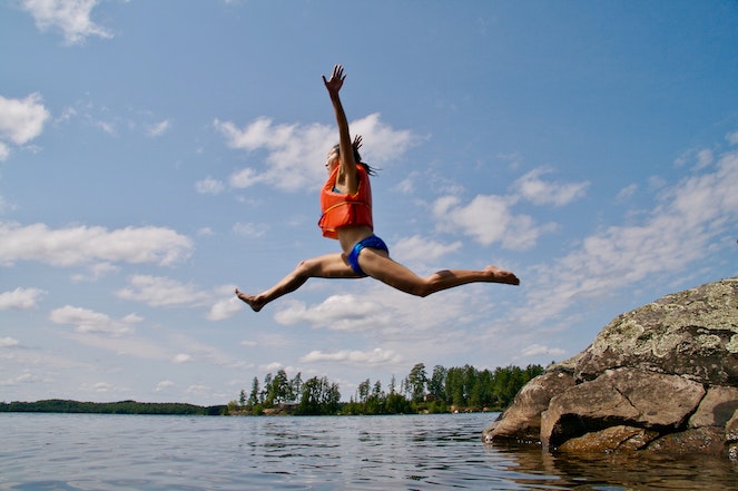 Young woman jumping off a rock into a lake in summertime