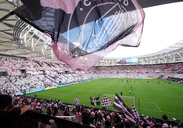Inter Miami fans waving large pink and black club flags inside the stadium as players warm up on the pitch before kickoff