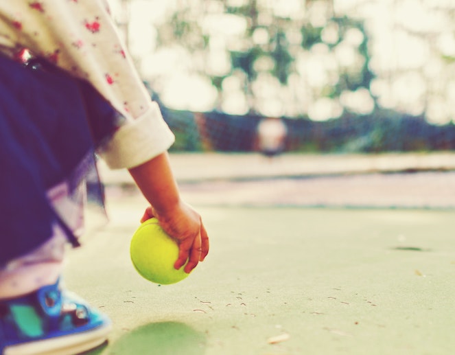 Young child picking up a tennis ball off the ground at an outdoor court