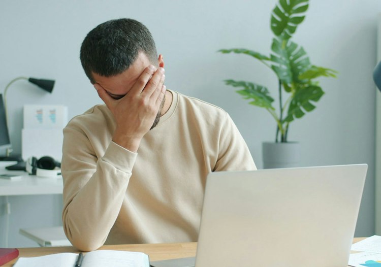 Frustrated man covering his face while looking at a laptop.
