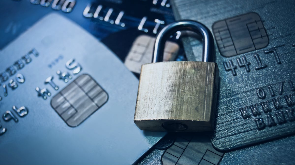 A brass padlock resting on a stack of credit cards, representing financial identity theft and payment card fraud.
