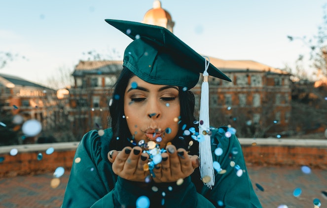 Young woman blows confetti at camera after graduating