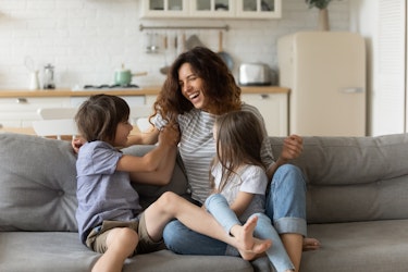 Joyful mother on the couch with her two children, smiling and playing. 