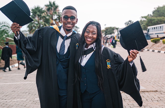 Young man and woman happily pose with cap and gown after graduating