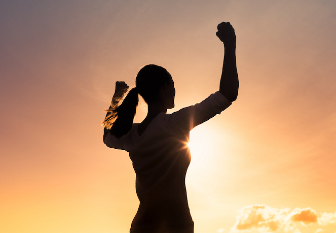 Confident female athlete with fists in the air looking into sun