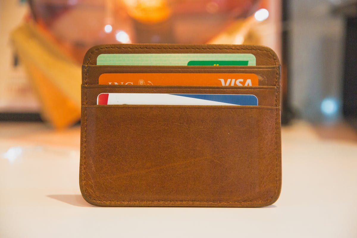 A brown leather card holder wallet standing upright, containing multiple cards including an ING Visa card and other colorful cards.