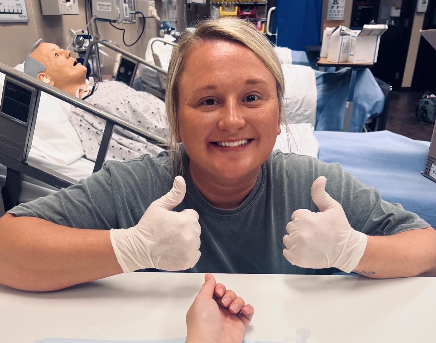 Morgan, a white woman with blond hair, wears light blue scrubs, a white long sleeve, stethoscope, and a bright smile.