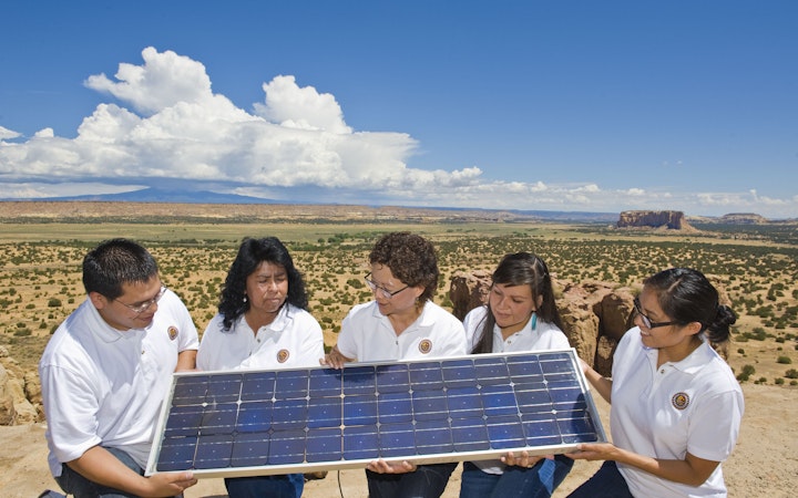 Sandra and her four interns holding a solar panel. Sandra explains how the solar panel generates renewable energy.