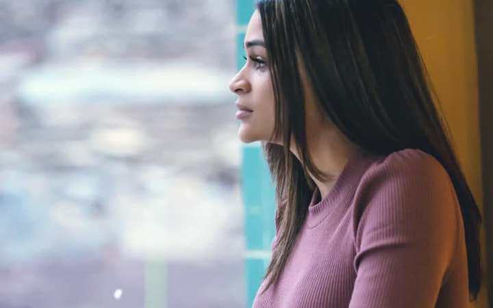 Leticia, a Hispanic woman dressed in a pink sweater, stares into the distance.