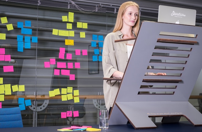 Woman working at standing desk with wall full of Post-its behind her