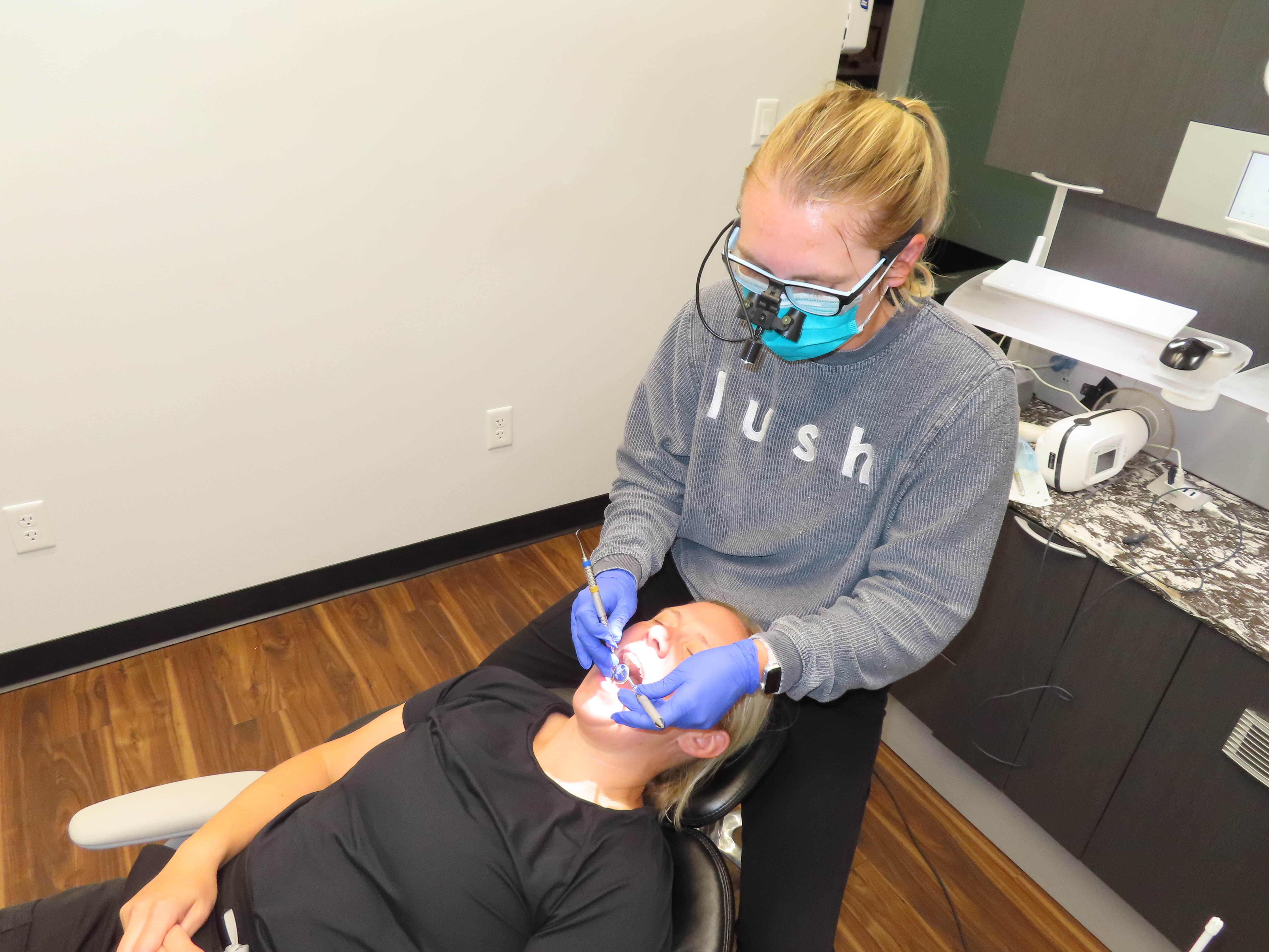 Shelby, a white woman with blond hair, wears her black lush dental scrubs and smiles.