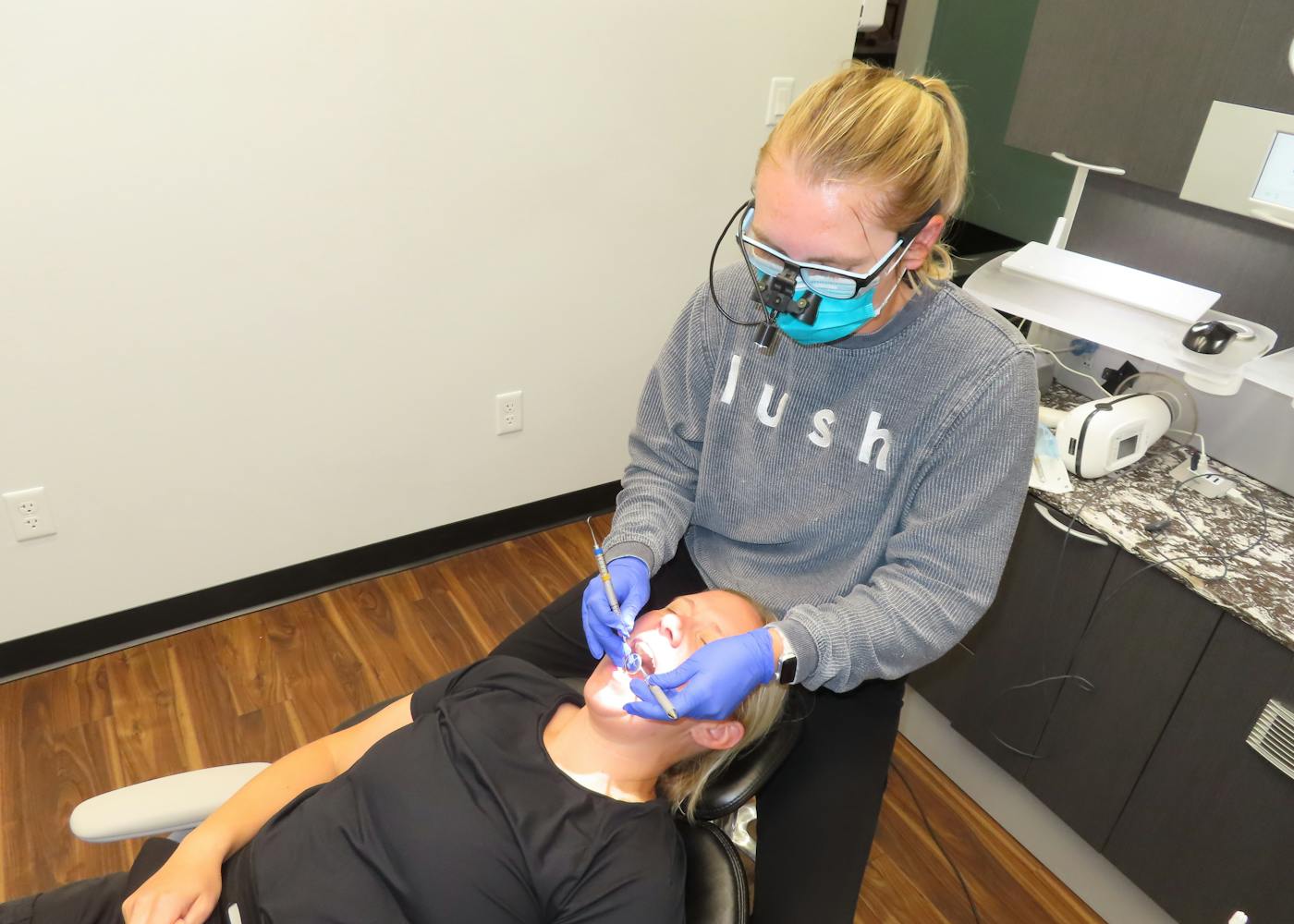 Shelby, a white woman with blond hair, wears her black lush dental scrubs and smiles.